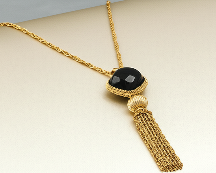 Gold necklace with a black pendant and tassel on a beige background