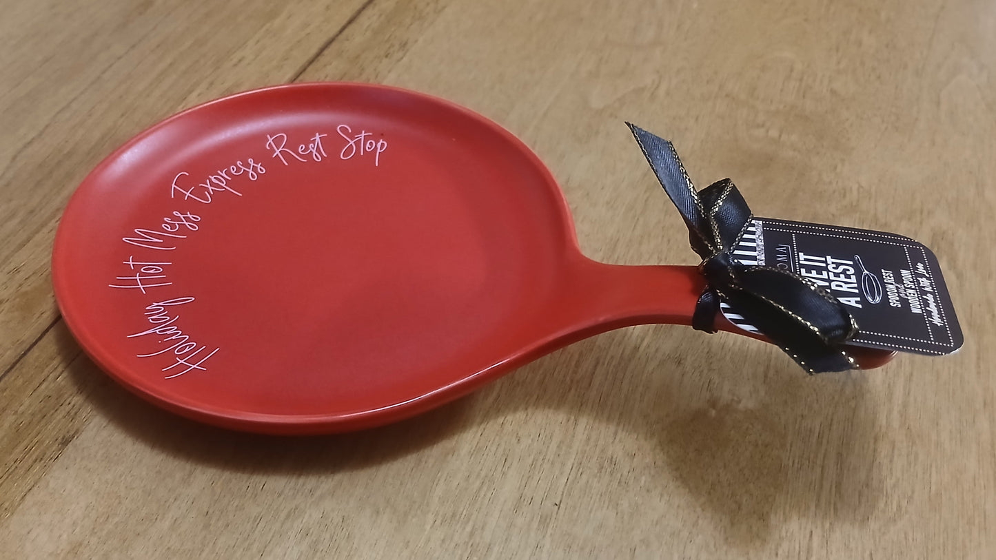 Red ceramic spoon rest with a black tag on a wooden surface