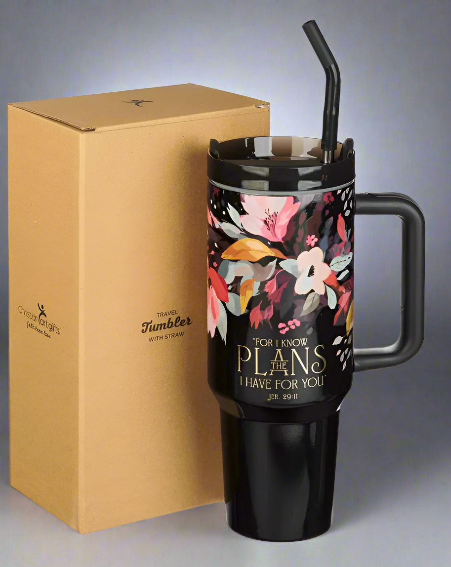 Floral-patterned travel mug with straw and handle next to a cardboard box on a white background
