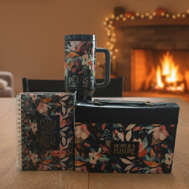Floral-patterned mug, notebook, and wallet on a wooden table with a fireplace in the background