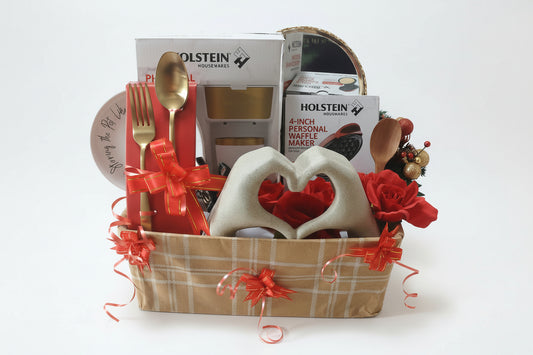Gift basket with waffle maker, heart-shaped spoons, and decorative items on a wooden table.