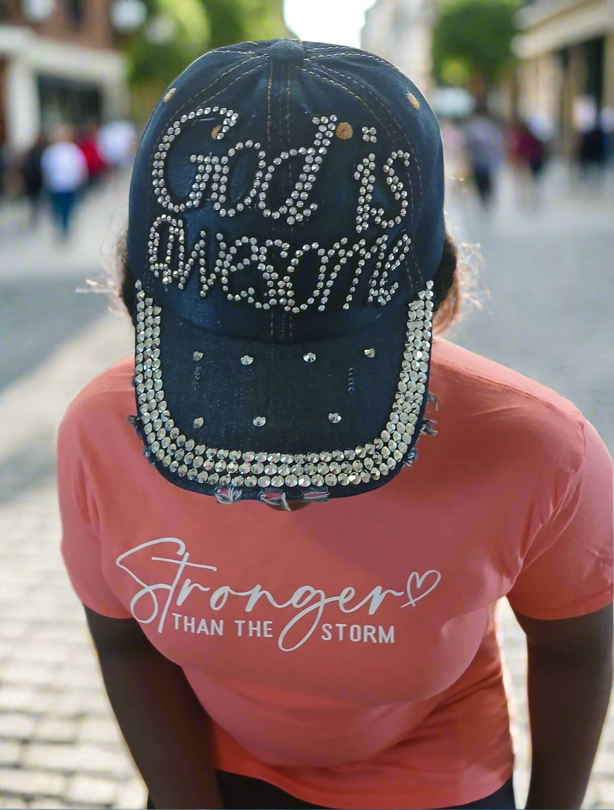 Person wearing a blue cap with 'God is awesome' and a pink shirt with 'Stronger Than The Storm' text.