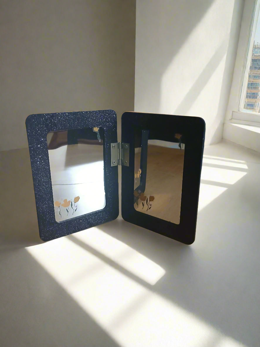 Two small rectangular frames on a light surface with sunlight casting shadows.